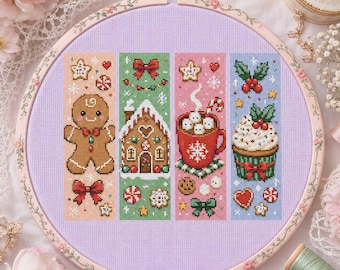 May include: A round wooden embroidery hoop containing a light purple fabric with four vertical cross-stitch patterns. The designs feature a gingerbread person, a gingerbread house, a mug of hot cocoa with marshmallows, and a decorated cupcake.