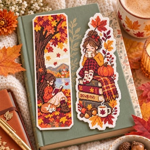 May include: Two rectangular cross-stitch bookmarks featuring autumn themes. One shows a person reading under a tree with falling leaves. The other depicts a person sitting on a stack of books with a pumpkin, a mug, and a maple leaf overhead.