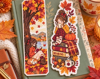 May include: Two rectangular cross-stitch bookmarks featuring autumn themes. One shows a person reading under a tree with falling leaves. The other depicts a person sitting on a stack of books with a pumpkin, a mug, and a maple leaf overhead.