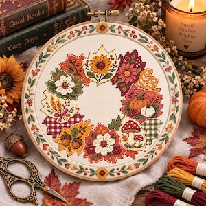 Peut inclure: Un tambour à broder circulaire contenant un motif au point de croix représentant une couronne d'automne. Le design présente des feuilles d'automne colorées, des tournesols, des citrouilles, des champignons et des motifs à carreaux.
