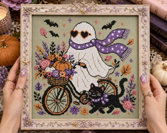 May include: A cross-stitch embroidery in a decorative frame featuring a white ghost wearing heart-shaped sunglasses and a purple star-patterned scarf, riding a bicycle with a basket of flowers and pumpkins, accompanied by a black cat and bats.