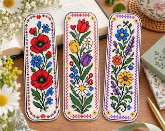 May include: Three rectangular bookmarks featuring intricate cross-stitch floral patterns. The left bookmark displays red poppies and blue flowers. The centre shows tulips and daisies. The right features sunflowers and purple lavender on white fabric.