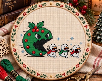 May include: A circular wooden embroidery hoop containing a cross-stitch design of a large green holly-themed character chasing three small snowmen. The hoop frame features a decorative border of green leaves and red berries on a cream fabric.
