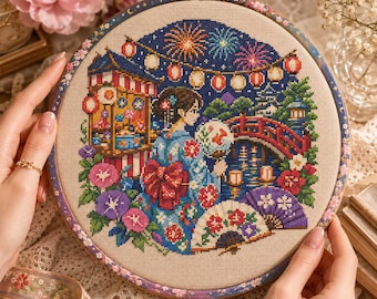 May include: A circular embroidery hoop containing a cross-stitch design of a person in a blue kimono holding a fan, standing before a red bridge, a festival stall, and fireworks. The scene includes colorful flowers and hanging paper lanterns.