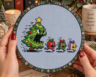 May include: A cross-stitch embroidery in a round wooden hoop featuring a light blue fabric background. The design depicts a large, angry green Christmas tree with a yellow star chasing three small, terrified, colorful gift boxes on legs.
