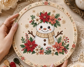 May include: A circular wooden embroidery hoop containing a cross-stitch design of a snowman wearing a tan scarf, surrounded by red and white poinsettias, green pine branches, and small gold snowflakes on a light beige fabric background.
