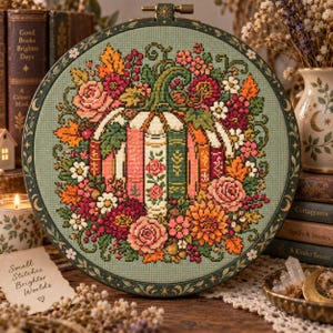 May include: A circular embroidery hoop containing a cross-stitch design of a pumpkin formed by stacked books, surrounded by colorful autumn flowers and leaves. The frame is dark green with gold moon and star accents on the outer edge.