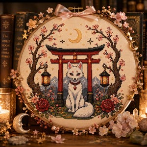 May include: A circular embroidery hoop featuring a cross-stitch design of a white fox sitting beneath a red torii gate. The scene includes cherry blossom branches, hanging lanterns, red roses, a yellow crescent moon, and a pink ribbon bow.