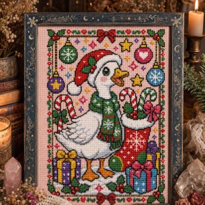 May include: A cross-stitch embroidery in a dark frame featuring a white goose wearing a red Santa hat and a green snowflake scarf. The goose stands beside a red Christmas stocking filled with candy canes and colorful wrapped gift boxes.