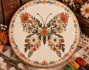 May include: A circular wooden embroidery hoop containing a cross-stitch design of a butterfly formed by orange, yellow, and white flowers with green leaves. The design is framed by a floral border on cream-colored fabric with a metallic screw top.