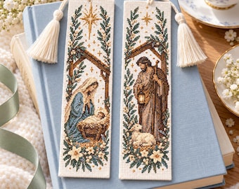 May include: Two rectangular cross-stitch bookmarks featuring nativity scenes. One shows a figure kneeling by a manger with a star above, the other shows a figure holding a lantern with a lamb. Both have cream fabric and white tassels.