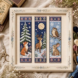 May include: Three vertical cross-stitch bookmarks framed in a light-colored wooden frame. The left bookmark shows a fox in snow with a pine tree. The center shows a deer under a full moon. The right shows an owl and a rabbit in a snowy scene.