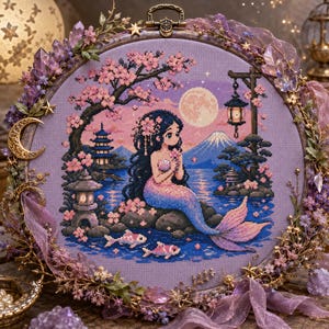 May include: A circular embroidery hoop featuring a cross-stitch design of a mermaid with long dark hair sitting on a rock by a lake. The scene includes cherry blossoms, a pagoda, a lantern, a full moon, and Mount Fuji, decorated with purple crystals.