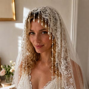 May include: A white lace bridal veil featuring intricate floral patterns along the edges and delicate strands of hanging teardrop-shaped pearls that drape over the forehead and down the sides, paired with a matching white lace sleeveless bodice.