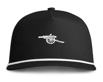 May include: A black baseball cap featuring a white embroidered graphic of a historical field cannon on the front panel. The cap includes a white cord trim running horizontally across the base of the crown, just above the flat brim.