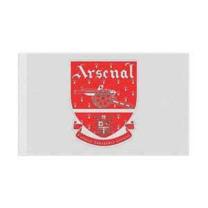 May include: A rectangular white flag featuring the red Arsenal football club crest in the center. The crest displays a white cannon, the word Arsenal in white gothic lettering, and a banner at the bottom with the text Victoria Concordia Crescit.