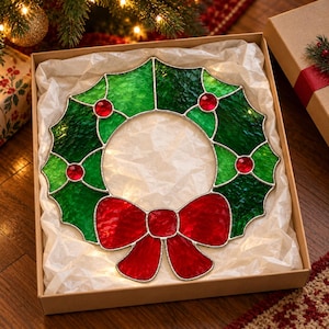 May include: A stained glass wreath ornament featuring textured green glass leaves and bright red glass berries, accented with a large red glass bow at the bottom. The piece is constructed with silver-toned metal soldering lines.