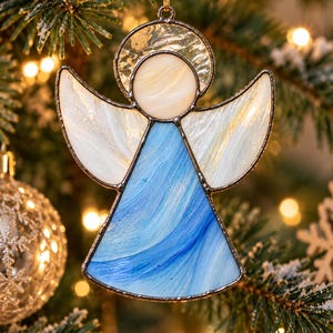May include: A stained glass angel ornament featuring a circular halo, white wings with subtle iridescent swirls, and a blue dress with flowing white streaks. The glass pieces are joined by dark metal solder lines and include a gold hanging loop.