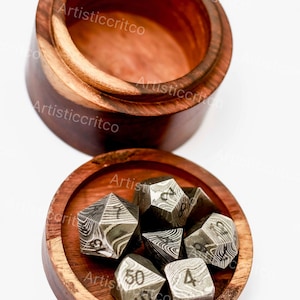 Puede incluir: Un juego de siete dados metálicos de múltiples caras con un patrón de remolinos gris oscuro y plateado, con números grabados, que descansan dentro de un recipiente redondo de madera marrón oscuro pulida con su tapa detrás.