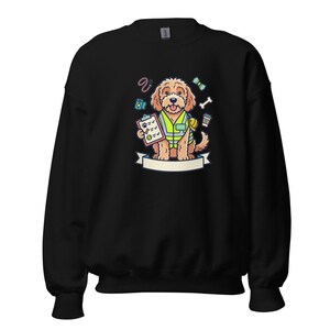 May include: Black sweatshirt with a cartoon dog wearing a yellow safety vest and holding a clipboard. The dog has a brown coat and is surrounded by illustrations of a bone, coffee cup, and other accessories. A white banner is below the dog.