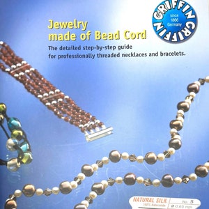 May include: Close-up of a spool of natural silk thread for stringing pearls and beads. The spool is labeled "Natural Silk 100% Naturseide" and "No. 5 0.65 mm".