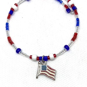 May include: A patriotic wrap bracelet featuring red, white, and blue beads, with a small American flag charm. The bracelet is made with clear, flexible wire and is designed to wrap around the wrist.