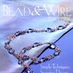 May include: A book cover with the title "Making Bead & Wire Jewelry" and the subtitle "Simple Techniques, Stunning Designs" by Dawn Cusick. The cover features a blue and silver beaded necklace on a blue and silver fabric background.