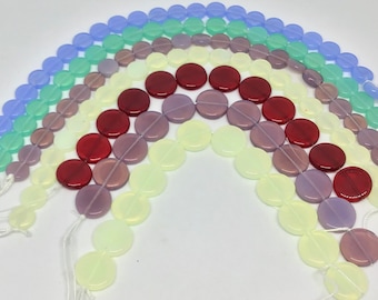 May include: A rainbow assortment of round glass beads, each strand featuring a different color: light blue, green, purple, red, and yellow. The beads are arranged in a semi-circle shape, creating a rainbow effect.