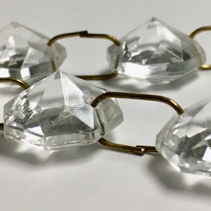 May include: A strand of clear crystal beads connected by gold-toned metal links. The beads are faceted and have a diamond-like shape.