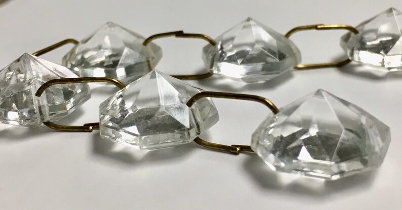 May include: A strand of clear crystal beads connected by gold-toned metal links. The beads are faceted and have a diamond-like shape.