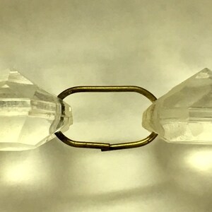May include: Close-up of a clear crystal bead with a faceted design, strung on a gold chain.