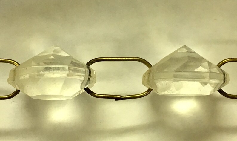 May include: Close-up of a clear crystal bead with a faceted design, strung on a gold chain.
