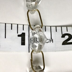May include: Close-up of a crystal bead chain with brass connectors. The chain is measured against a ruler, showing the beads are approximately 1 inch in diameter.