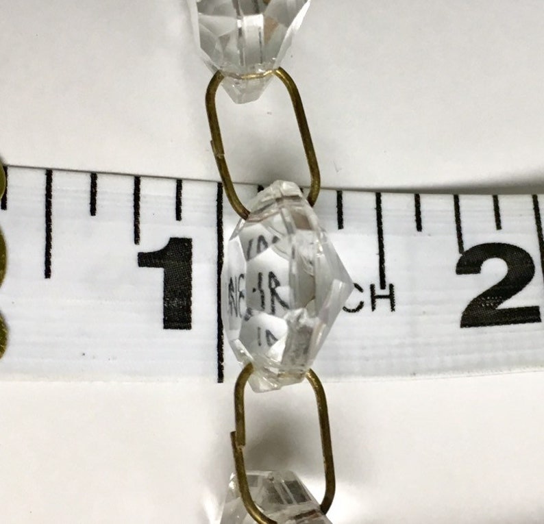 May include: Close-up of a crystal bead chain with brass connectors. The chain is measured against a ruler, showing the beads are approximately 1 inch in diameter.