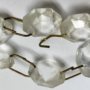 May include: A strand of clear glass crystal beads connected by gold metal links. The beads are faceted and have a slightly iridescent quality.