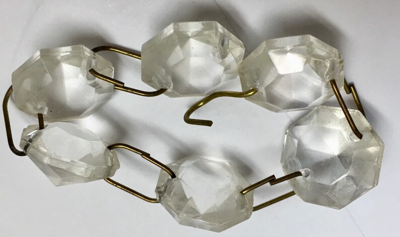 May include: A strand of clear glass crystal beads connected by gold metal links. The beads are faceted and have a slightly iridescent quality.
