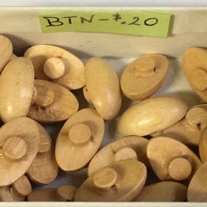 May include: A box filled with wooden buttons. The buttons are oval shaped with a small knob on top. The box has a yellow sticky note on it that says "BTN - $2.0"