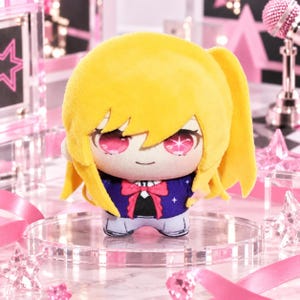 May include: A plush doll featuring bright yellow hair, large pink eyes with star-shaped highlights, and a small smile. The doll wears a dark blue jacket with a red bow tie and white accents, rendered in a soft, stuffed fabric construction.