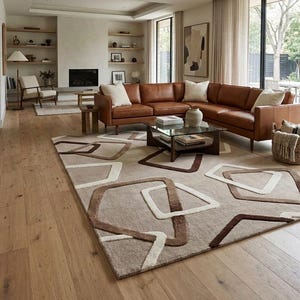 May include: A large rectangular area rug featuring a beige background with a repeating geometric pattern of interlocking brown and cream-coloured angular shapes. The rug is positioned on a light-coloured wooden floor in a living room setting.
