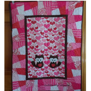 May include: A pink and white quilt with a brown border. The center of the quilt features a pink and white heart pattern with two brown foxes. The text "Quiltcountry/etsy.com" is in the bottom right corner.