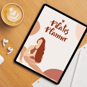 May include: A digital Pilates Planner on a tablet with a brown wooden background. The planner features the words "Pilates Planner" and an illustration of a person doing Pilates. A cup of coffee and wireless earbuds are also on the table.