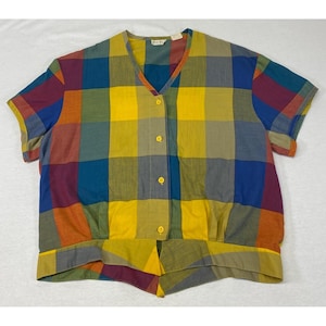May include: A short-sleeve button-down shirt featuring a vibrant multi-colored plaid pattern in shades of yellow, blue, green, and maroon. The shirt has a V-neckline, four yellow buttons down the front, and a gathered hemline at the waist.