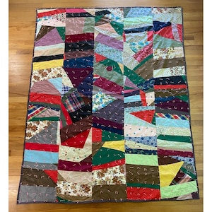 May include: A patchwork quilt with a variety of fabric patterns and colors, including floral, plaid, and solid hues. The quilt is rectangular and features a dark border. The fabrics are sewn together in a geometric design.