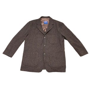 May include: A brown and black textured blazer featuring a notched lapel, three front buttons, two large patch pockets at the waist, and one chest pocket. The interior is lined with a solid brown fabric and includes a blue brand label at the neck.