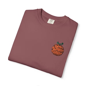 Op de afbeelding: Een mauvekleurig t-shirt met een kleine geborduurde afbeelding op de linkerborst. De afbeelding toont een ronde, oranje vrucht met een wervelend, vlamachtig patroon en een klein groen steeltje. Het shirt heeft een ronde hals en een binnenlabel.