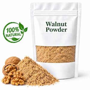 Op de afbeelding: Een witte stazak met het label Walnut Powder en een doorzichtig venster met lichtbruin poeder. Naast de zak ligt een hoopje van hetzelfde poeder, een hele walnoot en verschillende walnootkernen. Een groene stempel vermeldt 100% NATURAL.