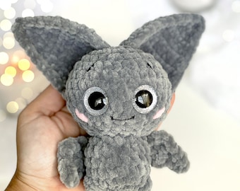 Può includere: Un piccolo pipistrello di peluche realizzato all'uncinetto con filato grigio morbido e soffice. Presenta grandi occhi rotondi neri con accenti glitter argento, piccole guance ricamate in rosa, una bocca cucita semplice e due grandi orecchie a punta.