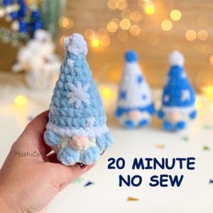 May include: A light blue and white crocheted gnome figurine with a pointed hat featuring snowflake patterns and a round peach-colored nose. The text 20 MINUTE NO SEW is visible in the lower right corner, and the brand name PlushiCo is on the left.