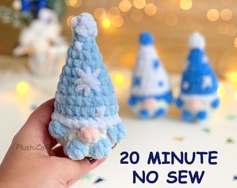 Può includere: Uno gnomo all'uncinetto azzurro e bianco con un motivo a fiocchi di neve sul cappello, naso rotondo e consistenza morbida. Il testo "PlushiCo" e "20 MINUTE NO SEW" è visibile, insieme ad altri due gnomi sfocati.