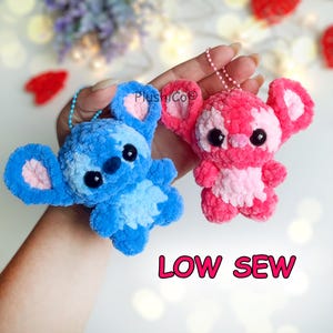 May include: Two plush keychains featuring a blue character and a pink character with large black eyes, rounded ears with light pink centers, and soft textured yarn. Each has a ball chain attached. The text PlushiCo and LOW SEW is visible.